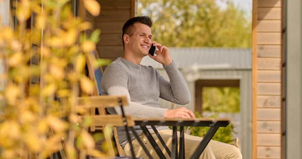Smiling man having a phone conversation while relaxing on an outdoor patio.